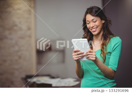Woman standing in lit room wearing bright green top and holding tablet above papers, copy space Woman standing in lit room wearing bright green top and holding tablet above papers, copy space 133291696