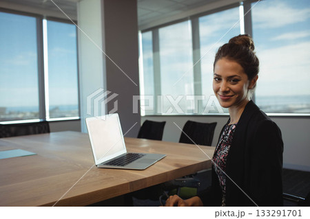 Woman wearing dark blazer working on laptop at conference room table with office chairs, copy space Woman wearing dark blazer working on laptop at conference room table with office chairs, copy space 133291701