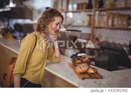 Woman in her 20s leaning toward wooden pastry board at countertop inside cafe, selecting croissant Woman in her 20s leaning toward wooden pastry board at countertop inside cafe, selecting croissant 133291702