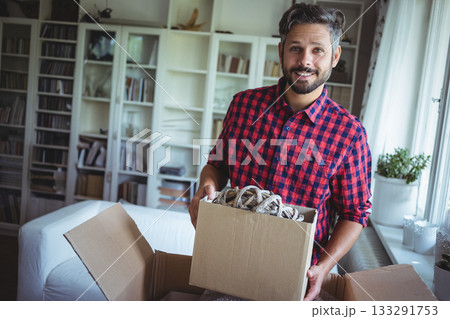 Man wearing flannel holding box with coiled ropes in living room by white shelves, copy space Man wearing flannel holding box with coiled ropes in living room by white shelves, copy space 133291753