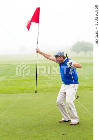 Senior African American man celebrating on putting green gripping flagstick and putter, copy space 133291969