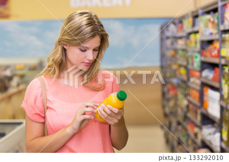 Fair-skinned woman checking label on orange juice bottle in bakery aisle near refrigerated counters Fair-skinned woman checking label on orange juice bottle in bakery aisle near refrigerated counters 133292010
