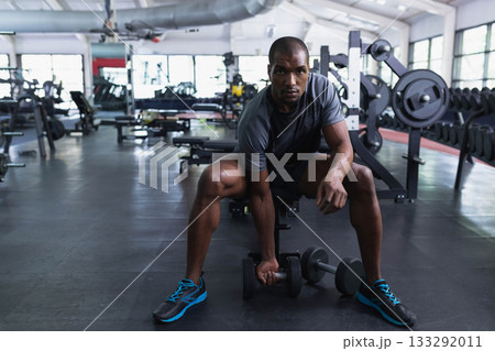 African American man picking up adjustable dumbbell from rubber gym flooring near weight bench African American man picking up adjustable dumbbell from rubber gym flooring near weight bench 133292011