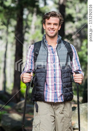 Male hiker wearing quilted vest smiling while trekking pine forest trail with poles and backpack Male hiker wearing quilted vest smiling while trekking pine forest trail with poles and backpack 133292016