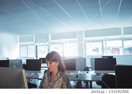 Mid-adult woman typing on keyboard at open-plan office desk, focusing on large monitor, copy space Mid-adult woman typing on keyboard at open-plan office desk, focusing on large monitor, copy space 133292068