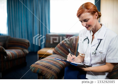 Red-haired female health worker writing on clipboard in lounge wearing white uniform, copy space Red-haired female health worker writing on clipboard in lounge wearing white uniform, copy space 133292085