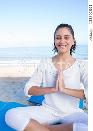 Woman meditating cross-legged on blue yoga mat on sandy beach by calm ocean waves, copy space Woman meditating cross-legged on blue yoga mat on sandy beach by calm ocean waves, copy space 133292091