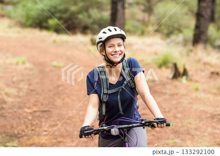 Woman cycling on purple bike wearing white helmet, hydration pack, cycling gloves on forest trail 133292100