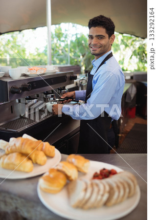 Man operating espresso machine behind outdoor cafe counter with pastry plates and cups, copy space 133292164