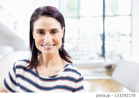 Female office worker smiling while standing in modern office near large windows and wooden table 133292170
