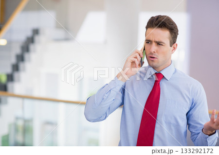 Businessman wearing red tie gesturing on smartphone by glass railing stairs in office, copy space 133292172
