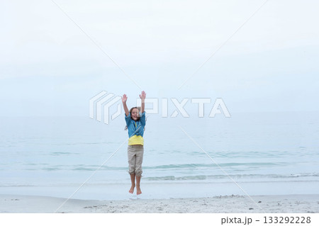 Female child jumping on sandy beach near calm sea under overcast sky wearing denim jacket Female child jumping on sandy beach near calm sea under overcast sky wearing denim jacket 133292228