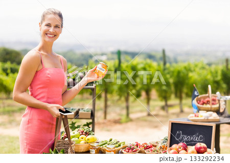 Female vendor smiling while holding organic jar and smartphone at vineyard market stall Female vendor smiling while holding organic jar and smartphone at vineyard market stall 133292234