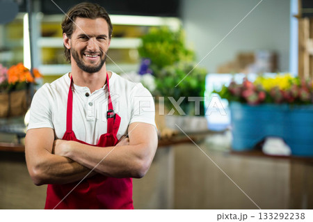 Male florist wearing red apron crossing arms at flower shop near buckets of blooms, copy space Male florist wearing red apron crossing arms at flower shop near buckets of blooms, copy space 133292238