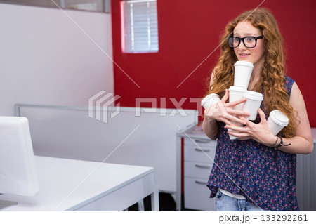 Woman wearing floral top balancing disposable coffee cups at office cubicle, copy space Woman wearing floral top balancing disposable coffee cups at office cubicle, copy space 133292261