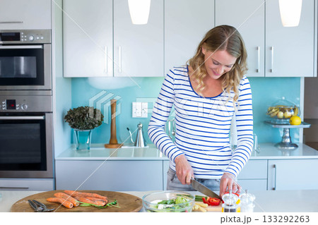 Woman chopping carrots and red bell pepper with chefs knife on countertop in kitchen, copy space Woman chopping carrots and red bell pepper with chefs knife on countertop in kitchen, copy space 133292263