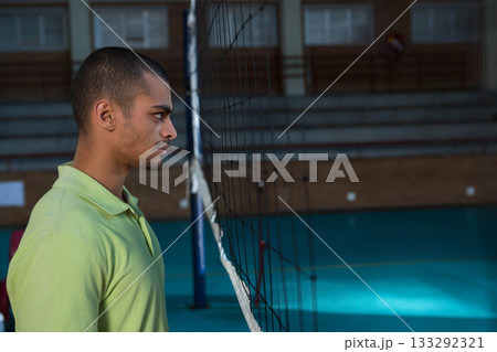 Man standing in profile scanning volleyball net at gym with green court, tiered seating, copy space 133292321