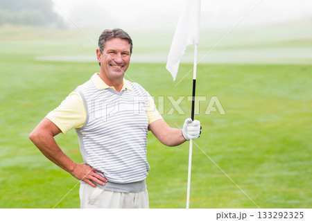 Senior African American man holding flagstick and smiling on putting green in vest and golf glove 133292325