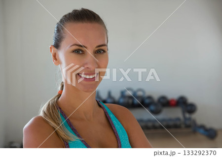 Female standing arms crossed in fitness studio next to kettlebell dumbbell rack, copy space Female standing arms crossed in fitness studio next to kettlebell dumbbell rack, copy space 133292370