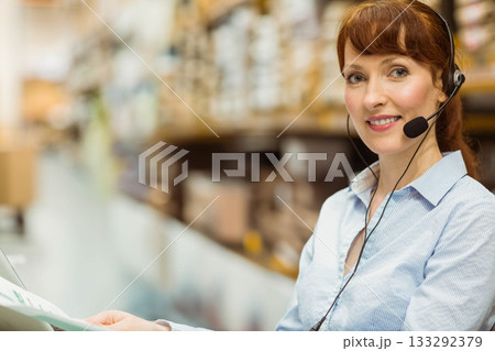 Woman call center agent holding printed documents and speaking into headset mic at desk, copy space Woman call center agent holding printed documents and speaking into headset mic at desk, copy space 133292379