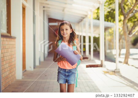 School-aged girl holding purple folder and carrying teal backpack on tiled floor under columns School-aged girl holding purple folder and carrying teal backpack on tiled floor under columns 133292407