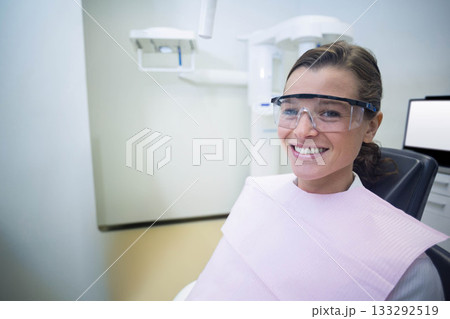 Female patient sitting in dental chair in examination room wearing goggles and bib, copy space 133292519