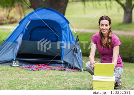 Woman wearing purple top kneeling at campsite next to yellow cooler by blue tent, copy space 133292551