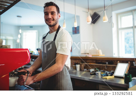 Male barista holding portafilter and operating touchscreen tablet behind counter in coffee shop 133292581