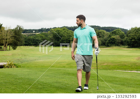 Man wearing golf attire walking across fairway with club, glove and shoes, copy space 133292593