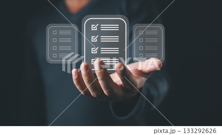 A person holds a digital interface displaying three floating icons representing a checklist document with checkboxes and lines, symbolizing digital tasks, workflow, and organization efficiency. A person holds a digital interface displaying three floating icons representing a checklist document with checkboxes and lines, symbolizing digital tasks, workflow, and organization efficiency. 133292626