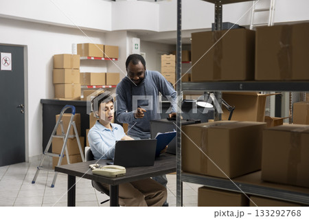 Multiethnic team of workers at a depot fulfillment center managing local shipping and inventory processes, working together in a warehouse full of taped boxes and storage shelving units. Multiethnic team of workers at a depot fulfillment center managing local shipping and inventory processes, working together in a warehouse full of taped boxes and storage shelving units. 133292768