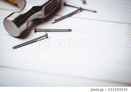 Claw hammer head is resting on white painted wooden surface in 3D render with scattered nails Claw hammer head is resting on white painted wooden surface in 3D render with scattered nails 133293545