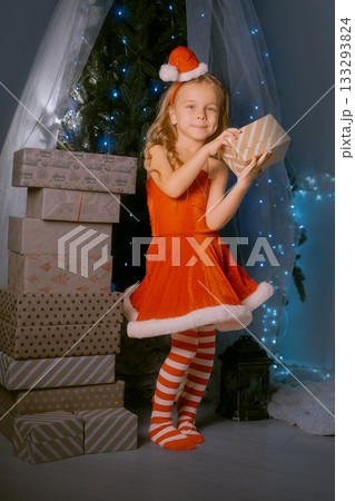 Holiday celebration with a girl in a red Santa outfit holding a Christmas gift surrounded by sparkling decorations. 133293824