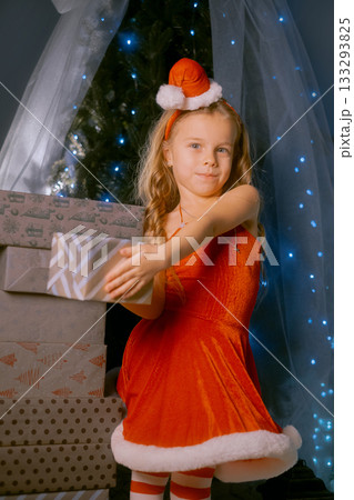 Elegant young woman dressed as Santa Claus enjoying the festive season next to a decorated Christmas tree. 133293825