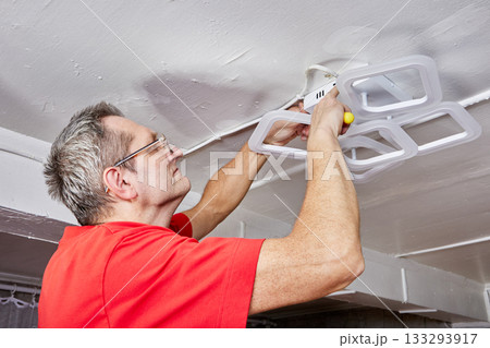 Electrical mounting task involves technician connecting LED chandelier to ceiling in country home as part of lighting installation process. 133293917