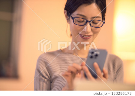 リビングで仕事をしながらスマホを見るミドル女性 133295173