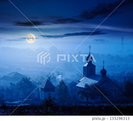 old church in the village in autumn at night. view of countryside landscape from a hill in haze and full moon light. empty rural fields. background for investment or abstract concepts 133296313