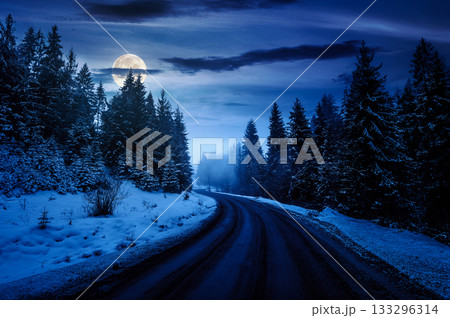 country road winding through spruce forest in winter at night. spooky nature landscape on foggy weather in full moon light. transportation background. backdrop for fiction art or mystery concepts 133296314