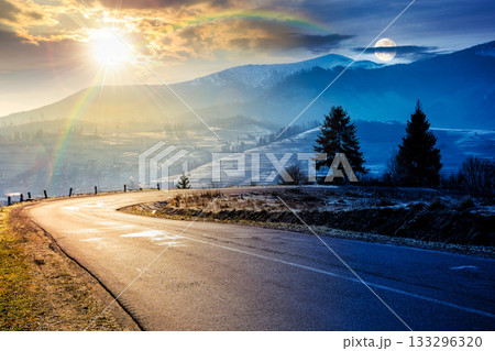 country road in mountains. day and night time change concept. beautiful countryside landscape in late autumn. fir trees on the roadside with sun and moon. scenic view of distant ridge in snow 133296320