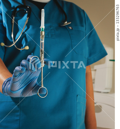 The dentist, in a blue lab coat and gloves, holds a carpal syringe in front of him, 133296763