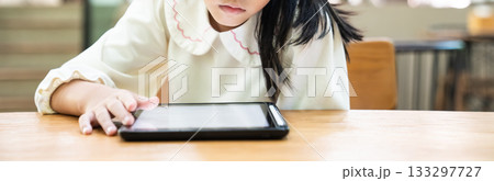 A young child leans closer to the tablet while gently tapping the screen with full attention with a calm moment of exploration and early learning. A young child leans closer to the tablet while gently tapping the screen with full attention with a calm moment of exploration and early learning. 133297727