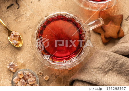 Black tea in transparent glass cup on brown textured table background with cookies and ingredients. Cozy breakfast teatime, top view Black tea in transparent glass cup on brown textured table background with cookies and ingredients. Cozy breakfast teatime, top view 133298567