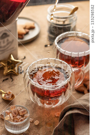 Pouring black tea into transparent glass cup from teapot on brown textured table background. Frozen spalshes of tea in cup 133298582
