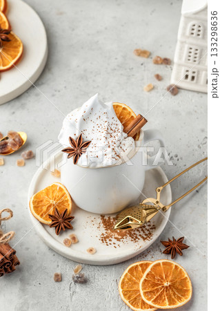 Hot cocoa drink with whipped cream, dried orange and spices in mug on white festive christmas table background Hot cocoa drink with whipped cream, dried orange and spices in mug on white festive christmas table background 133298636