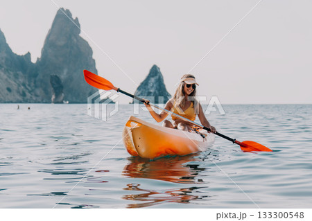 Kayaking Woman Sea - A woman in a yellow bikini paddles a kayak in the ocean with a rocky mountain range in the distance. 133300548