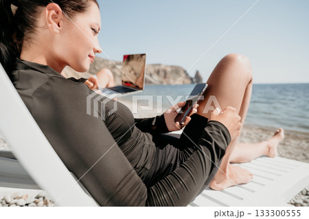 Woman Beach Phone Relaxing Seashore - A young woman is relaxing on a beach, looking at her phone on a sunny day. Woman Beach Phone Relaxing Seashore - A young woman is relaxing on a beach, looking at her phone on a sunny day. 133300555