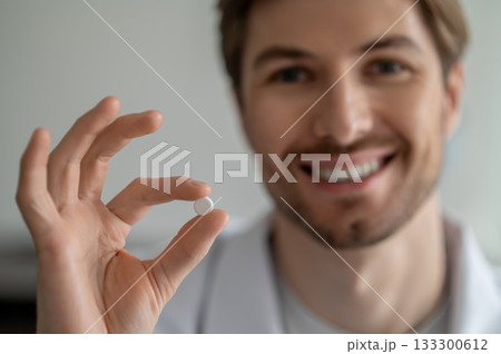Close-up of smiling man's hand holding small white pill Close-up of smiling man's hand holding small white pill 133300612
