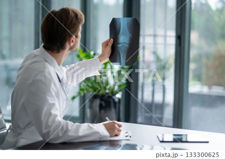Doctor with stubble and lab coat examining x-ray at desk Doctor with stubble and lab coat examining x-ray at desk 133300625