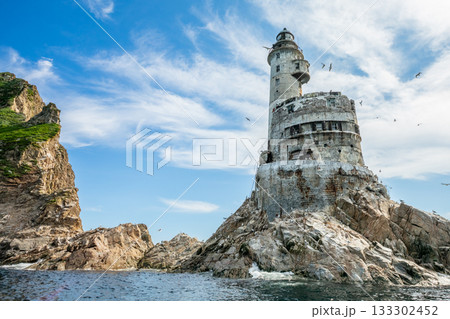 Former Japanese Aniva Lighthouse on a remote rocky island off the coast of Sakhalin, Russia. The abandoned tower shows visible decay, rust and erosion, standing above strong waves in a harsh marine 133302452