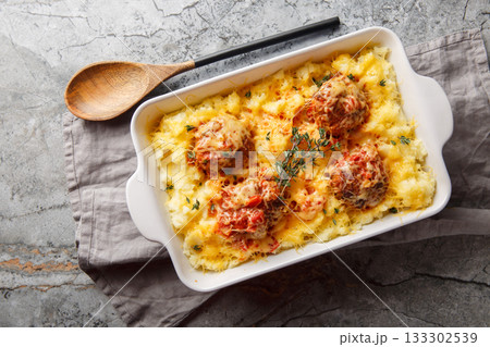 Hot mashed potatoes with Italian meatballs baked with cheese and herbs close-up in a baking dish. Horizontal top view 133302539